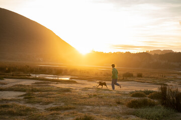 a woman playng with her dog at sunset