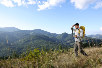 Fototapeta na wymiar Tourist with backpack and trekking poles enjoying mountain landscape, space for text