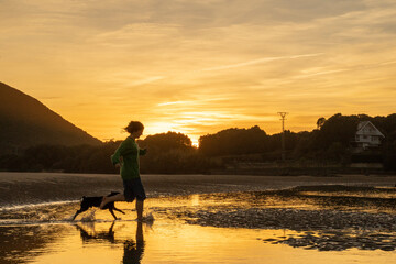 girl playing with her little black dog in the water under sunset light