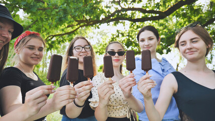 Girlfriends hold chocolate ice cream on a stick in a row.