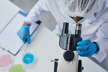 High angle view of African scientist in protective wear looking through the microscope and examining new virus in the lab