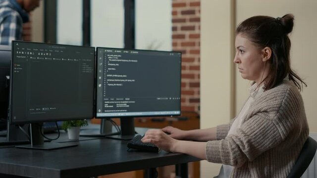 Portrait of focused programer writing code looking at multiple computer screens displaying programming language algorithm. Software developer coding while colleagues doing teamwork in background.