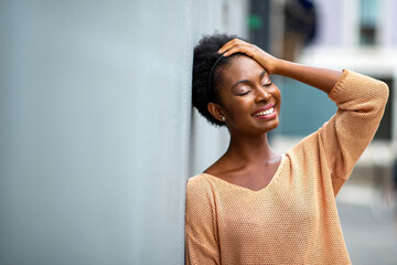 smiling young black woman leaning against wall with eyes closed