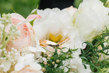 Golden wedding rings and a beautiful wedding bouquet of roses and eustoma in the background close-up. Details and wedding traditions.