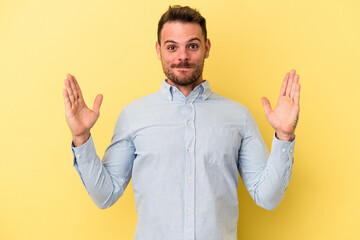 Young caucasian man isolated on yellow background holding something little with forefingers, smiling and confident.