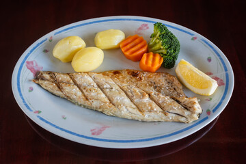 Grilled sea bass file with baked potatoes and vegetables in plate on the table. Traditional Portuguese dish.