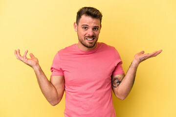 Young caucasian man isolated on yellow background doubting and shrugging shoulders in questioning...