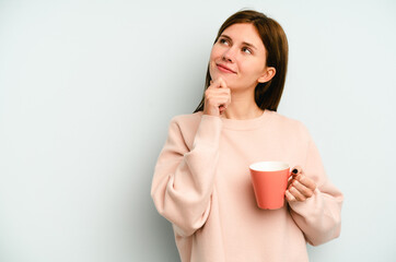 Young English woman holding a mug isolated on blue background looking sideways with doubtful and skeptical expression.