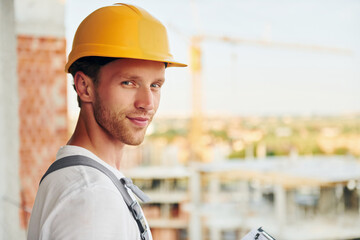 View from the side. Young man working in uniform at construction at daytime