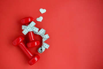 Two red dumbbells, white measuring tape, hearts on red background with copy space. Concept of...