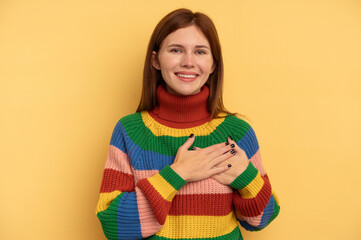 Young English woman isolated on yellow background has friendly expression, pressing palm to chest. Love concept.