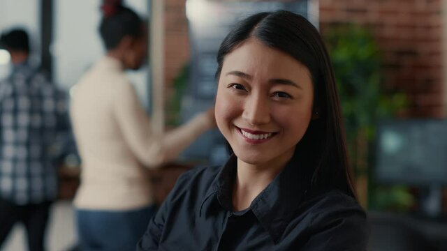 Portrait of smiling asian software developer looking at camera in cloud computing development agency. Confident programer posing happy next to colleagues working in big data office.