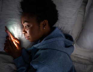 Top of young African American woman looking at cellphone in bed