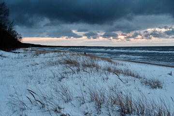 dark clouds over sea on a cold winter sunset evening snow on beach