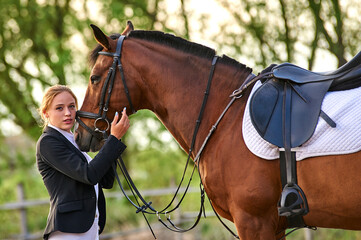 Beautiful horse rider girl stands near a horse on a farm
