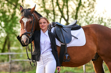 Beautiful horse rider girl stands near a horse on a farm
