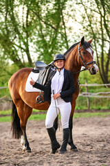 Beautiful horse rider girl stands near a horse on a farm
