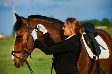 Beautiful horse rider girl stands near a horse on a farm
