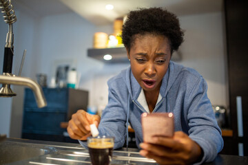 Obraz na płótnie Canvas young black woman sitting at table with coffee holding mobile phone