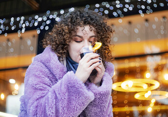 Selective focus. Beautiful woman holds mulled wine. Festive decorations outdoors.
