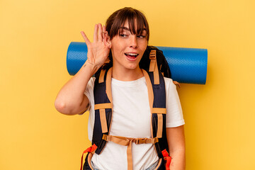 Young Argentinian hiker woman isolated on yellow background trying to listening a gossip.