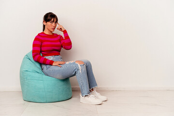 Young Argentinian woman sitting on a puff isolated on white background pointing temple with finger, thinking, focused on a task.