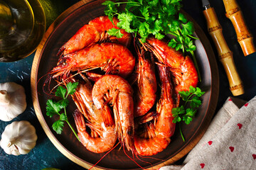Top view of grilled shrimps and lemon pieces on plate with arranged spices around on black surface