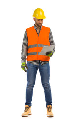 Worker in orange reflective waistcoat and white helmet is standing with documents and looking at it.