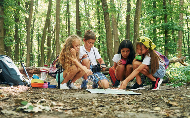 Sitting on the ground. Kids strolling in the forest with travel equipment