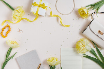 Workspace of a fashion blogger: yellow flowers, spring tulips, cosmetics, women's handbag, gift box with a bow. Flat lay, copy space