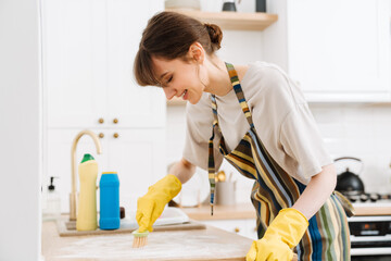 White young woman in gloves cleaning table with brush