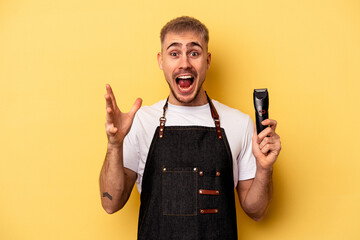 Young caucasian hairdresser man isolated on yellow background receiving a pleasant surprise, excited and raising hands.