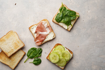 White toasts with cream cheese, ham, cucumbers and spinach