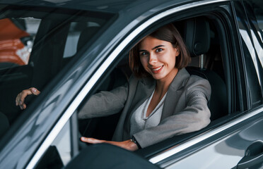 Black colored vehicle. Woman testing new car. Sitting indoors in modern automobile