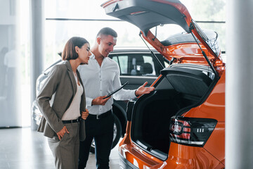 Standing near the car. Man in formal wear helping customer with choice of the automobile