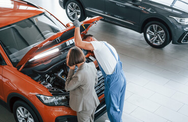 Woman talking by phone. Man repairing automobile indoors. Professional service
