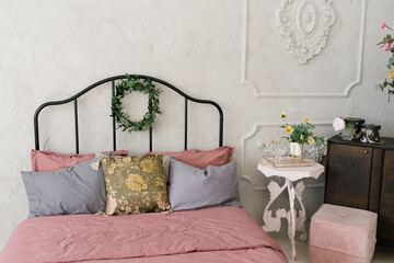 Bed with pink linens and gray pillows, a wreath of leaves on the bed