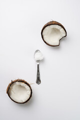 Cracked open coconut and a tea spoon with coconut oil on a white surface