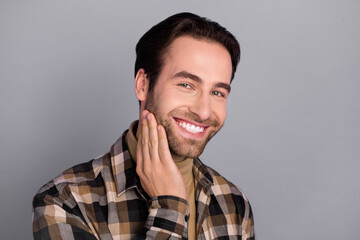 Portrait of attractive well-groomed cheerful guy wearing checked shirt touching face beard isolated over grey color background