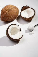 Fototapeta na wymiar Cracked open coconut and a tea spoon with coconut oil on a white surface