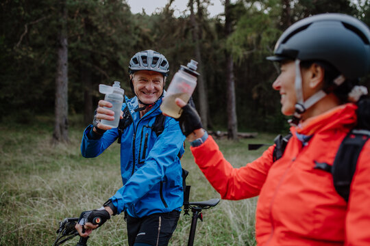 Happy senior couple bikers with wtaer bottles outdoors in forest in autumn day.