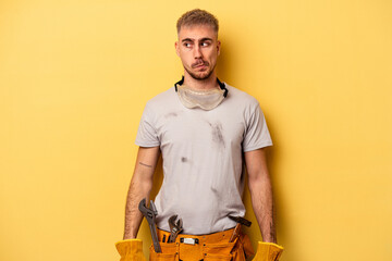 Young electrician caucasian man isolated on yellow background confused, feels doubtful and unsure.