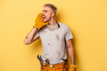 Young electrician caucasian man isolated on yellow background shouting and holding palm near opened...
