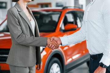 Doing handshake. Man in formal wear helping customer with choice of the automobile