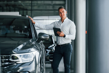 Fototapeta na wymiar Man in formal clothes is standing indoors near moden new car