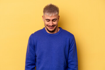 Young caucasian man isolated on yellow background laughs and closes eyes, feels relaxed and happy.