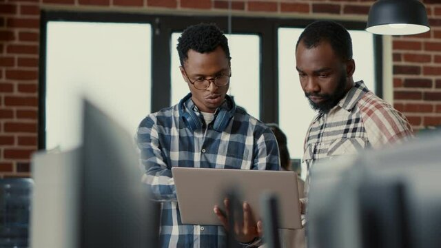 Coders talking about algorithms holding laptop pointing at sorce code on screen standing in software developing office. Team of coders discussing cloud computing in programming enviroment.
