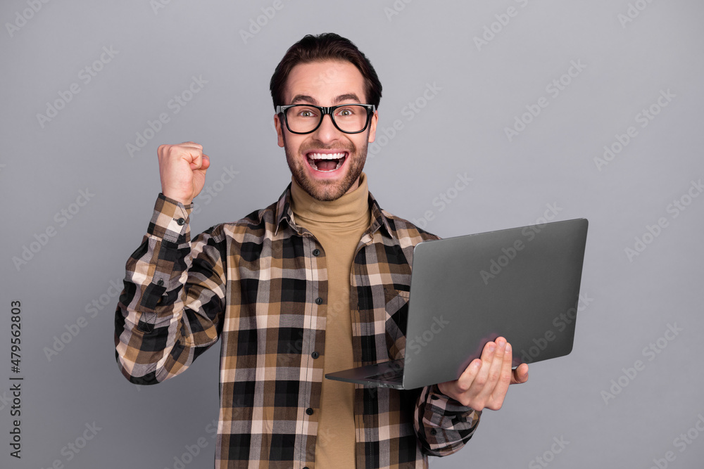 Poster Photo of cheerful lucky man wear plaid shirt spectacles rising fist holding gadget isolated grey color background