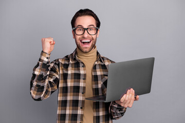 Photo of cheerful lucky man wear plaid shirt spectacles rising fist holding gadget isolated grey color background