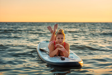 A sexy adult tanned woman in red swimsuit lie on sup board at the sea. Copy space. The concept of...